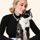 Smiling woman holding her tuxedo cat, both in matching faux pearl necklaces