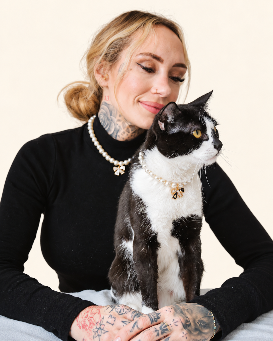 Smiling woman holding her tuxedo cat, both in matching faux pearl necklaces