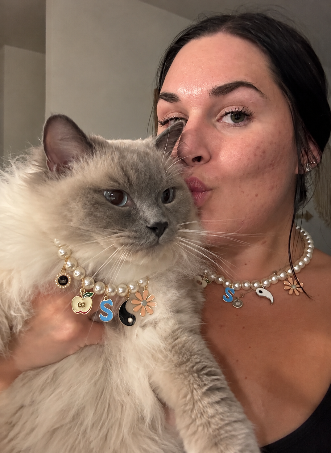Woman and her fluffy Ragdoll cat wearing matching pearl necklaces with colorful charms