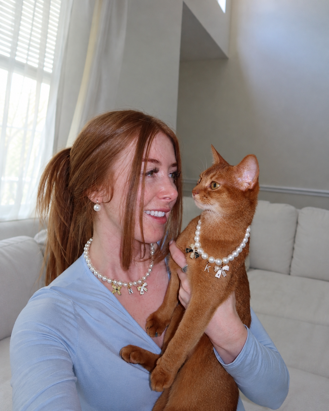 Woman holding her Abyssinian cat, both wearing matching faux pearl necklaces