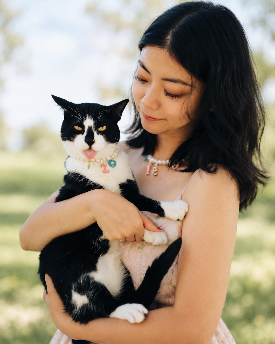 Woman outdoors holding her tuxedo cat, both in matching freshwater pearl necklaces