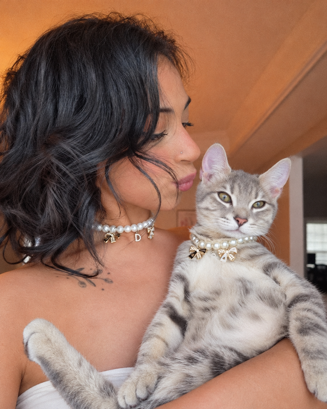 Woman holding her tabby cat, both wearing matching freshwater pearl necklaces with charms
